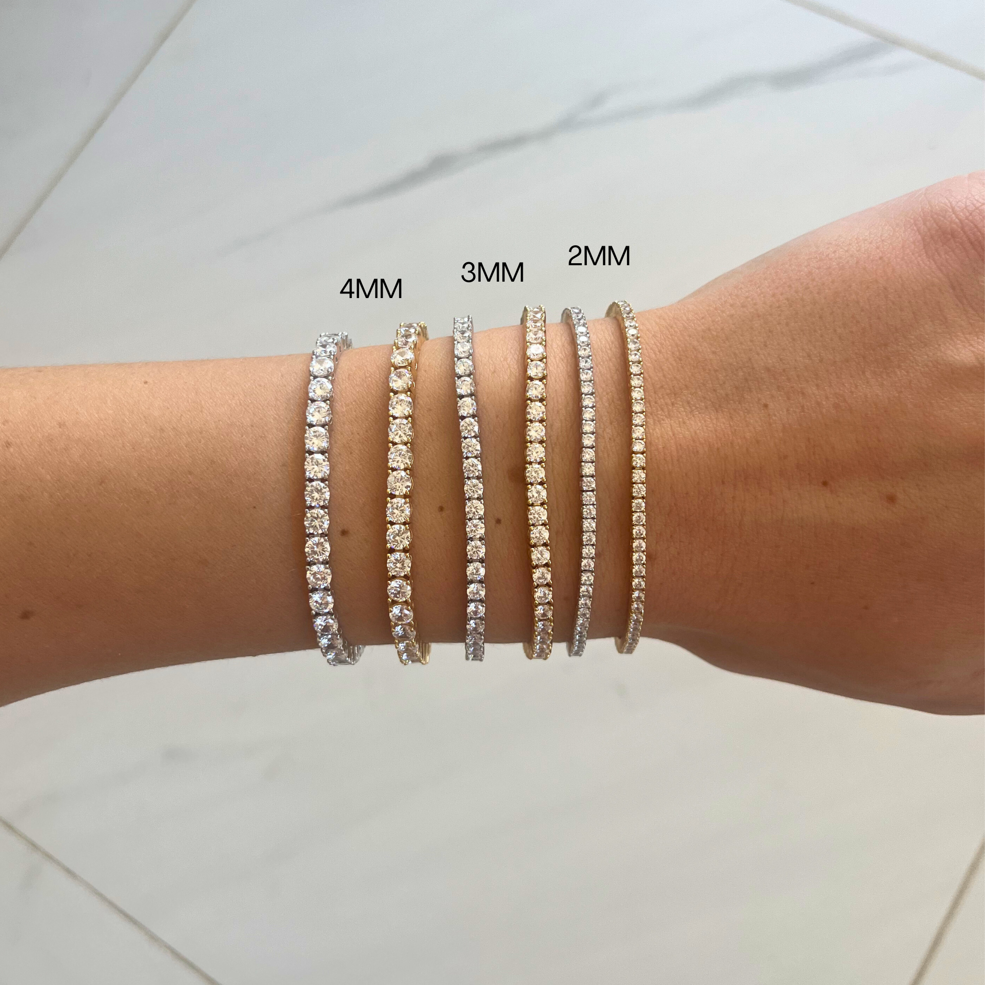 Stack of diamond tennis bracelets on a wrist with size labels.