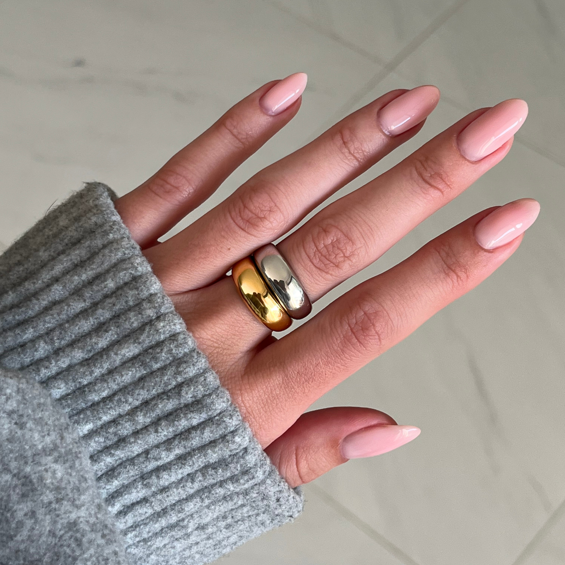 Hand wearing two gold rings with a neutral background