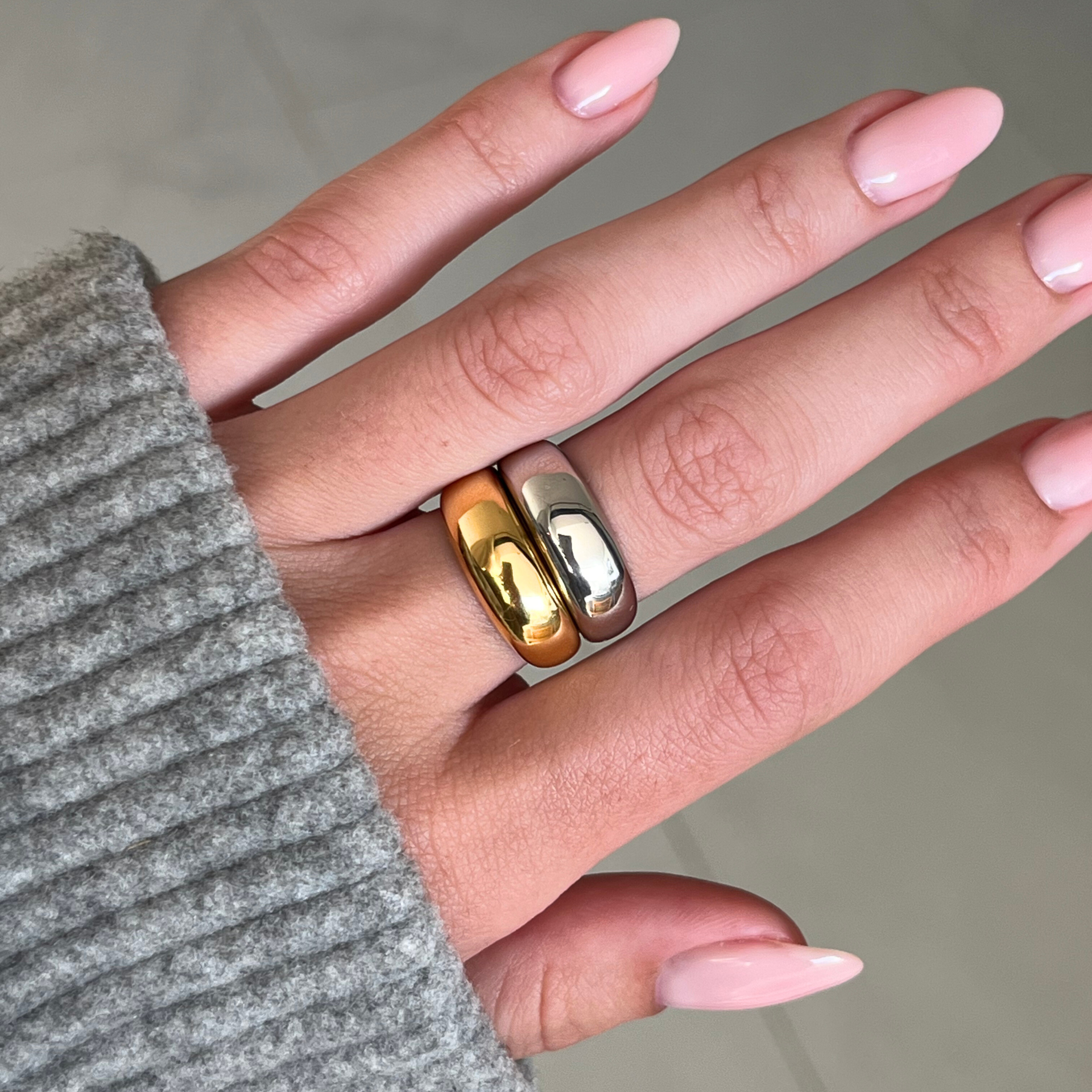 Hand wearing two gold rings with a neutral background