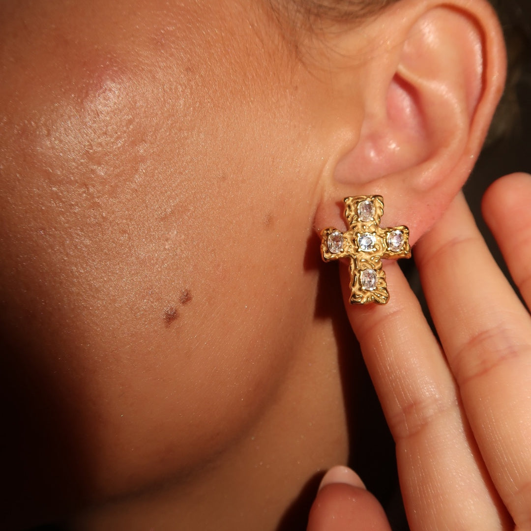 Close-up of a person wearing gold multi-gemstone cross style earrings.