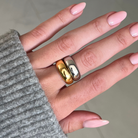 Hand wearing two gold rings with a neutral background