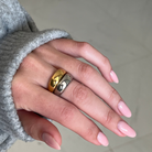 Hand wearing two gold rings with a neutral background