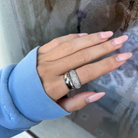 Hand wearing a silver ring with a textured band, against a blurred background.