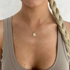 Woman wearing a gold necklace with a square pendant against a neutral background