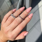 Hand with pink nail polish wearing two rings, one silver and one rose gold, against a blurred background.